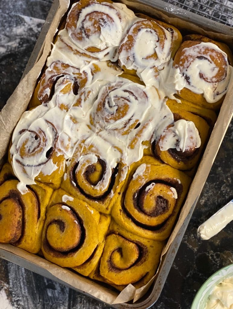 Maple Pumpkin Cinnamon Rolls with Maple Cream Frosting partially spread on Pure Maple